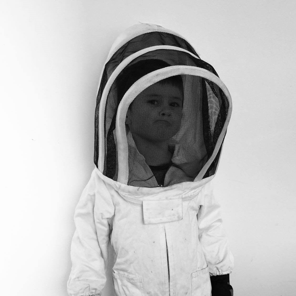 A boy dressed in a white protective beekeepers suit pulls a funny face.